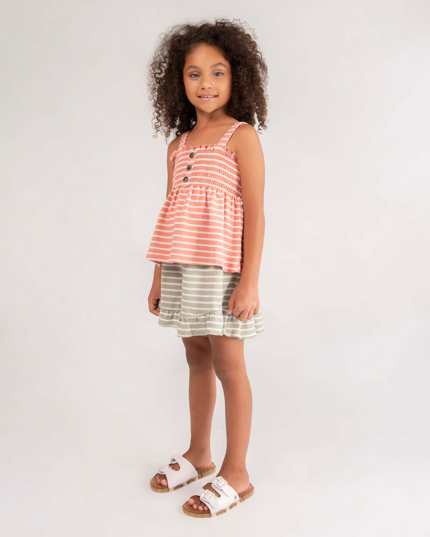 A young model in a dress, wearing a pair of Beige Mini Melissa Wide Slides with a white top with two white buckles and a beige sole.