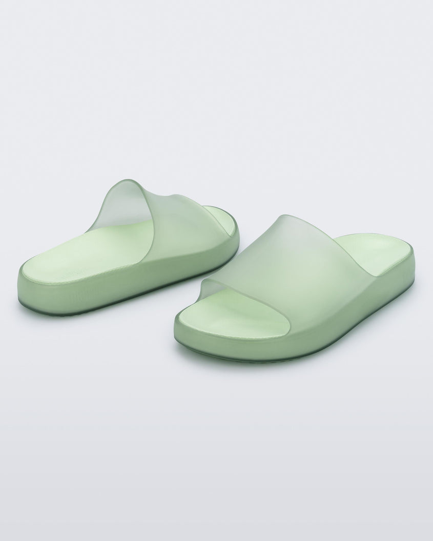 An angled side front and back view of a pair of transparent green Melissa Cloud slides.