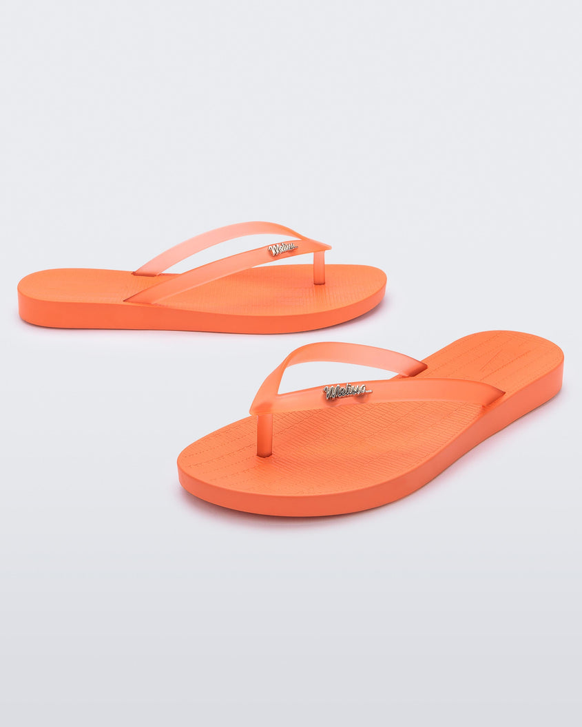 An angled front and side view of a pair of orange Melissa Sun Venice flip flops with 