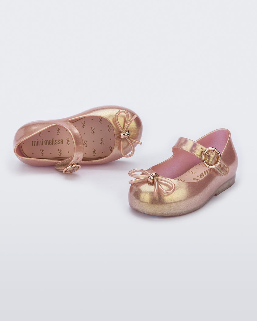 An angled front and top view of a pair of pink Mini Melissa Sweet Love flats with a top strap and a bow detail on the toe.