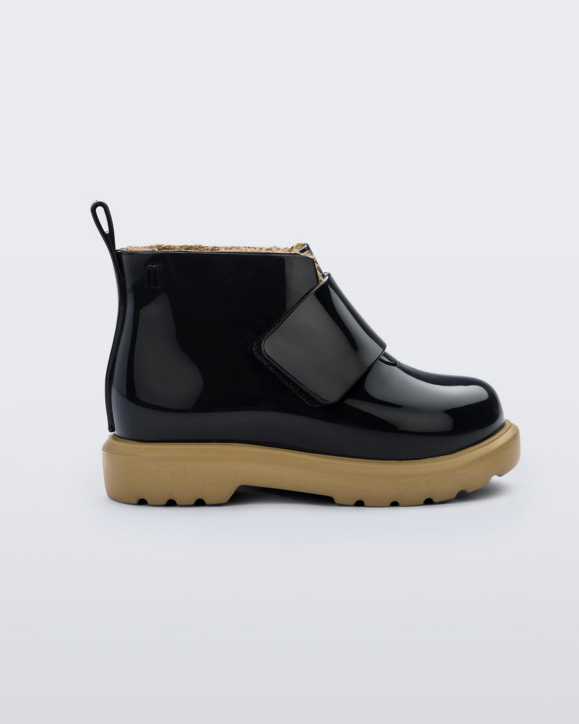 An outter side view of a black/beige Mini Melissa Chelsea boot with a black base, velcro front strap and beige sole.