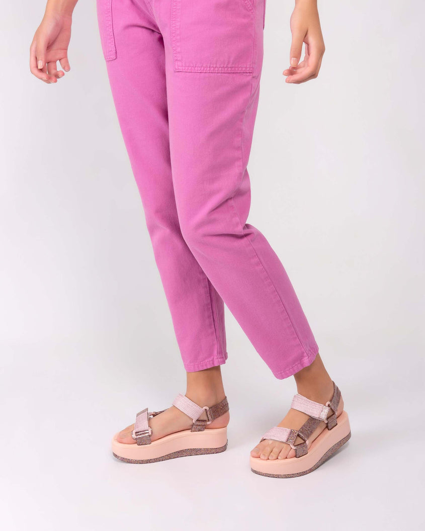 A model's legs in pink pants and a pair of a Melissa Papete Platform sandals with glitter straps and a pink and glitter sole.