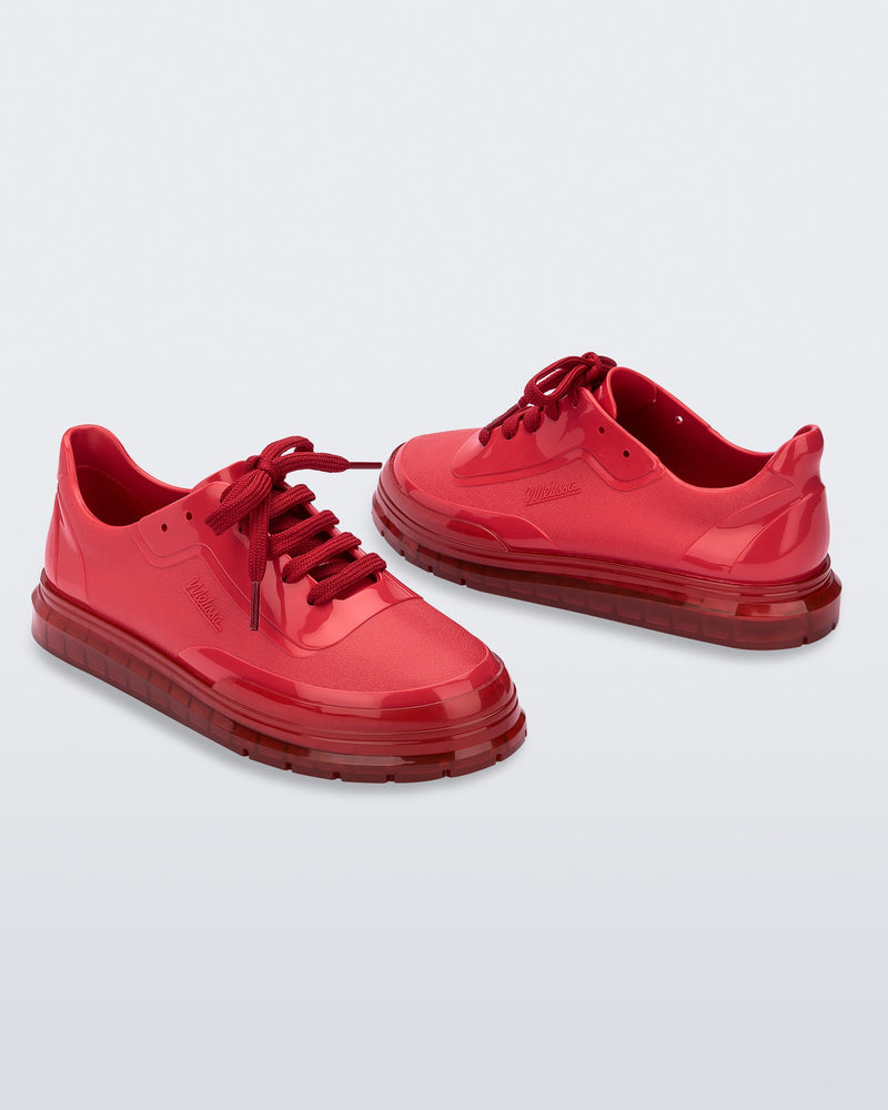 An angled front and side view of a pair of red Melissa Classic sneakers with a red base, laces, sole and a melissa logo on the side.