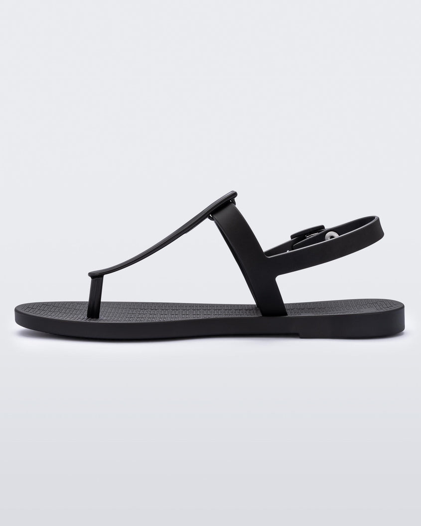 An inner side view of a pair of black Melissa Sun Ventura sandal with a top strap, reading melissa in silver, intersected by a vertical front strap detail and an ankle strap.