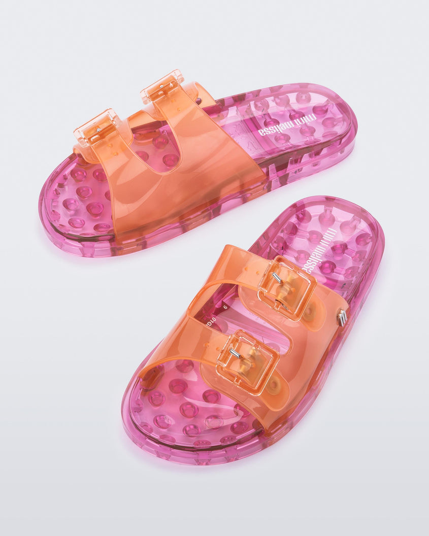 An angled top view of an orange/pink Mini Melissa Wide Slides with an an orange top with two silver buckles and a pink sole.