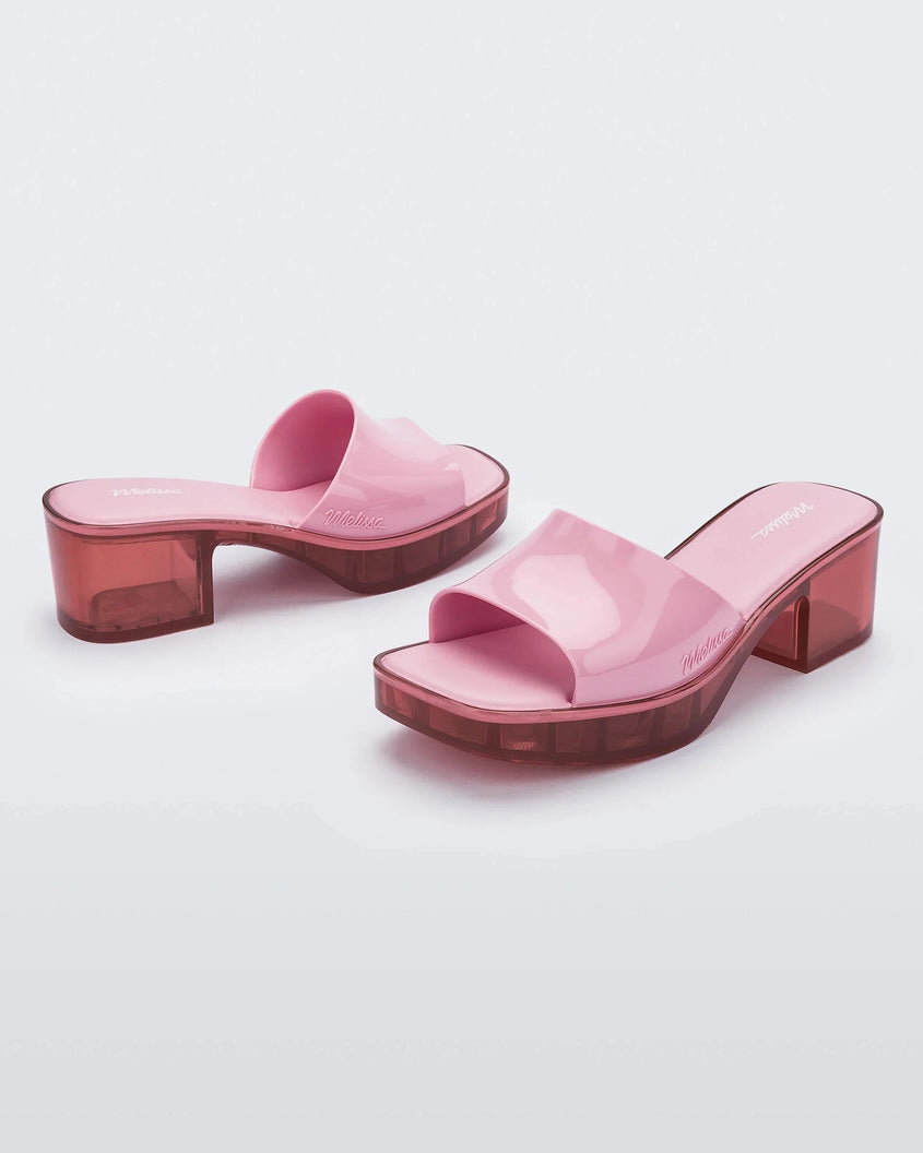 Angled view of a pair of Melissa Shape slides with transparent pink platform heel and a pink wide front strap. 