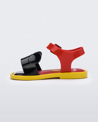 An inner side view of a red Mini Melissa Mar Sandal with mickey mouse insole, a red top strap, black bottom strap with mickey mouse ears on the top and a yellow sole.