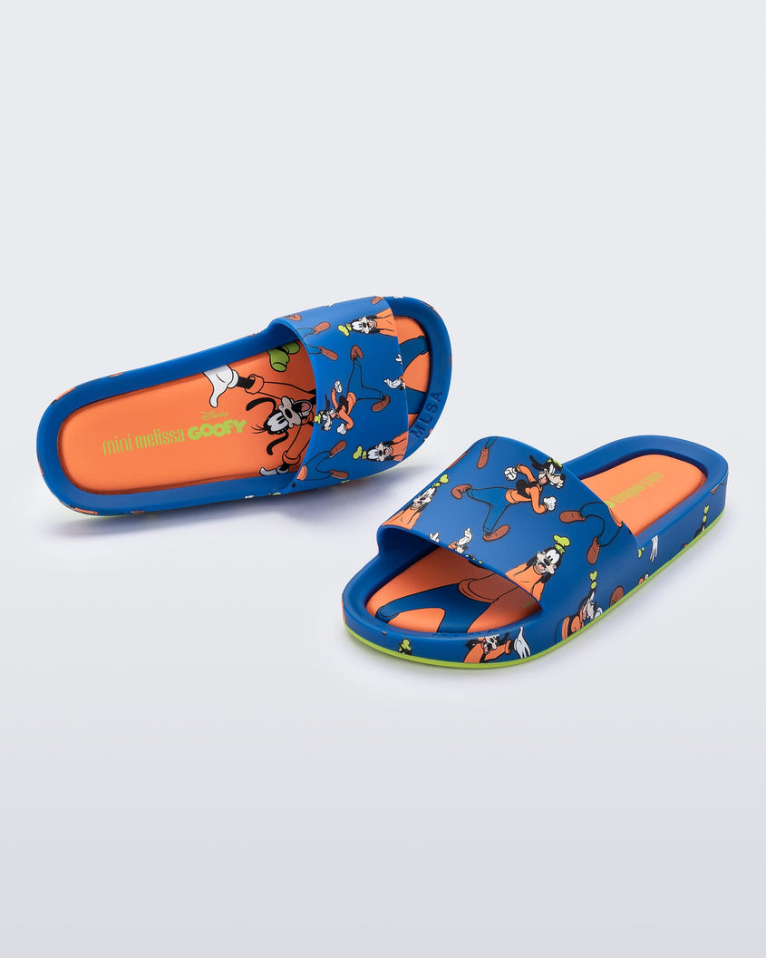 An angled front and top view of a pair of blue Mini Melissa Beach slides with a blue base and a pattern of Disney's Goofy in different poses.