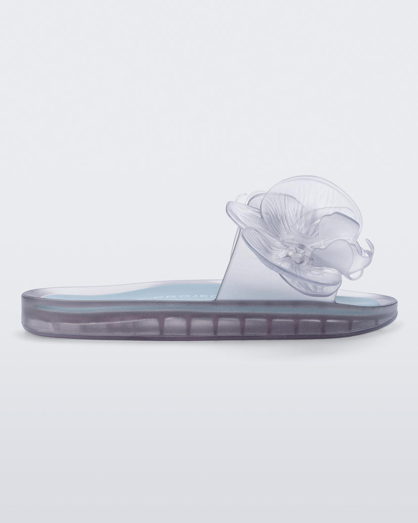 Side view of a Melissa Flower Beach slide in Clear with 3D flower on the strap.