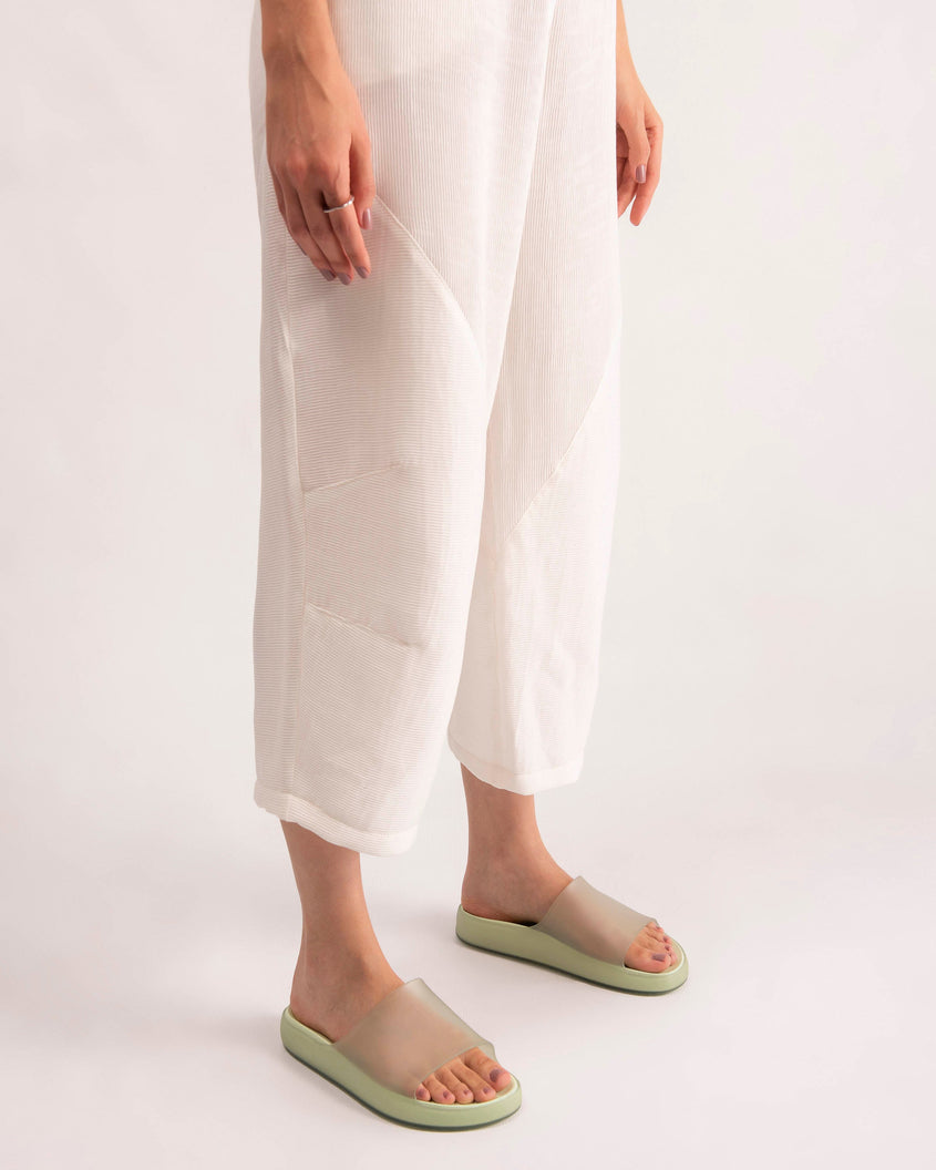 A model's legs wearing white pants and a pair of transparent green Melissa Cloud slides.