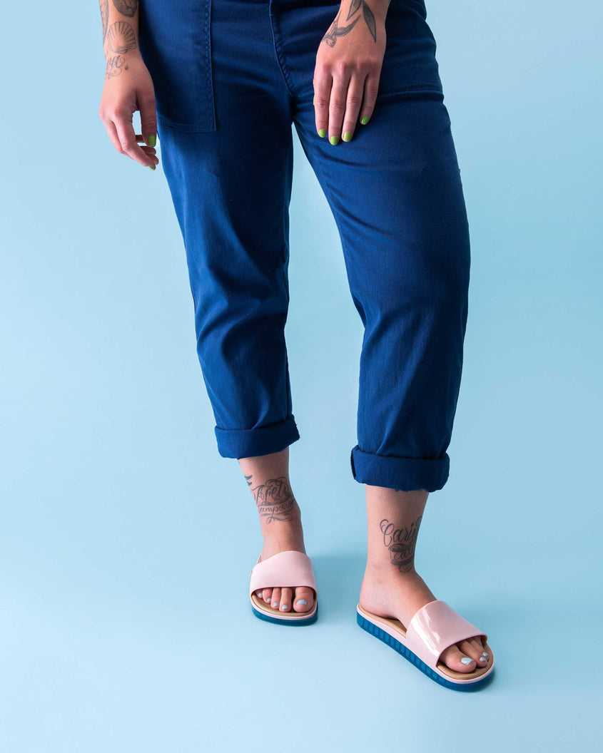 A model wearing a pair of pink Melissa Beach slides with blue soles. 