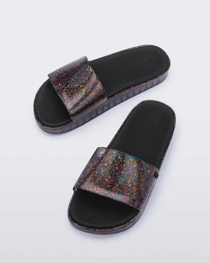 Angled view of a pair of clear/glitter Melissa Beach slides. 