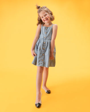 A young model in a gray dress, wearing a pair of white Mini Melissa Sweet Love Cap Toe flats with a white base and a black toe cap with a bow on top.