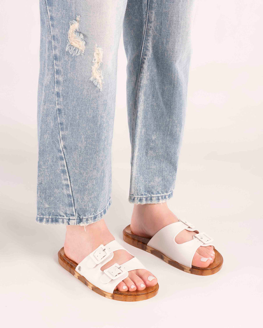 Model's legs wearing a pair of Melissa Wide slide sandals with gold glitter sole and white double straps with buckles