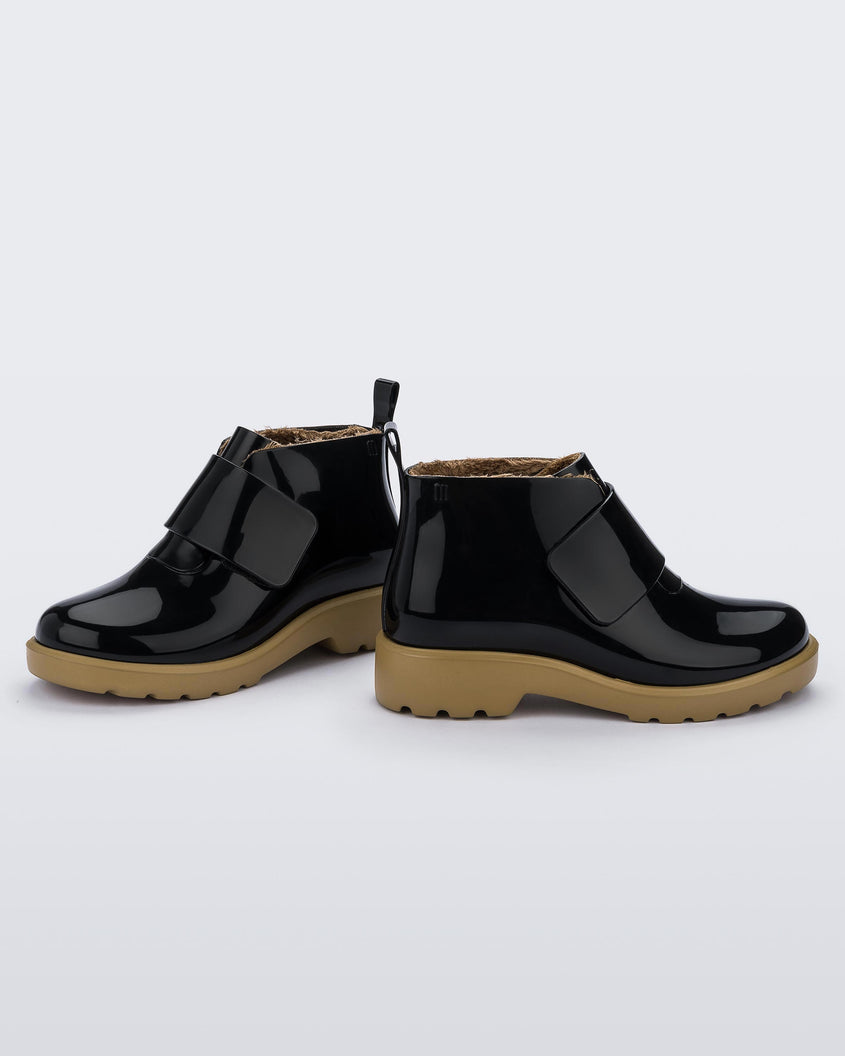 Side view of a pair of black/beige Mini Melissa Chelsea boots with a black base, black velcro front strap and beige sole.