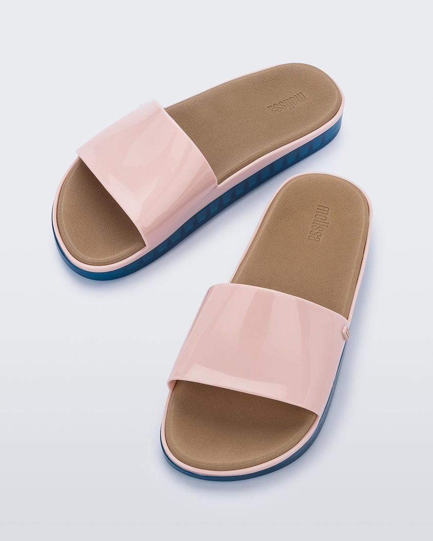 Angled view of a pair of pink Melissa Beach slides with blue soles. 
