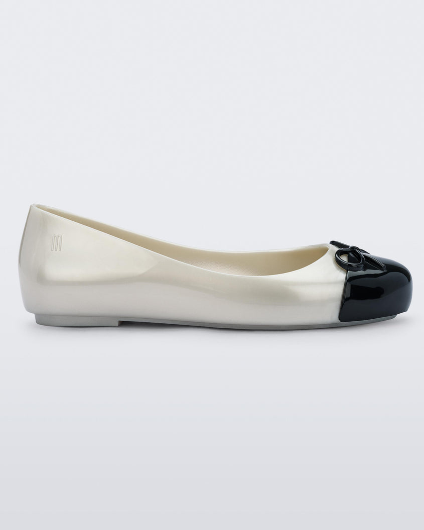 An outter side view of a white Mini Melissa Sweet Love Cap Toe flat with a white base and a black toe cap with a bow on top.