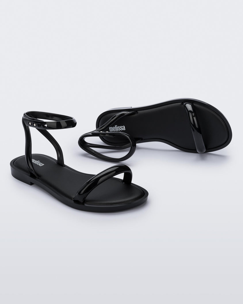 An angled side and top view of a pair of black Melissa Wave Sandal with one front strap and one ankle strap.