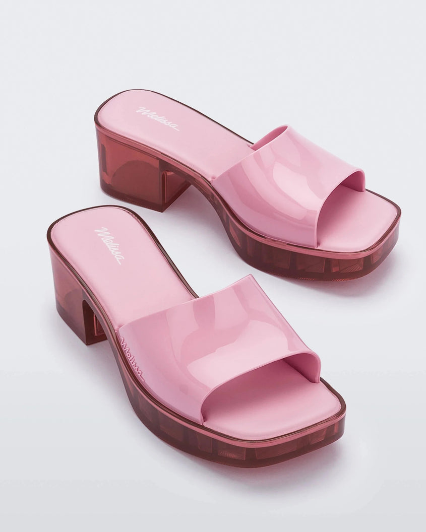 Additional angled view of a pair of Melissa Shape slides with transparent pink platform heel and a pink wide front strap. 