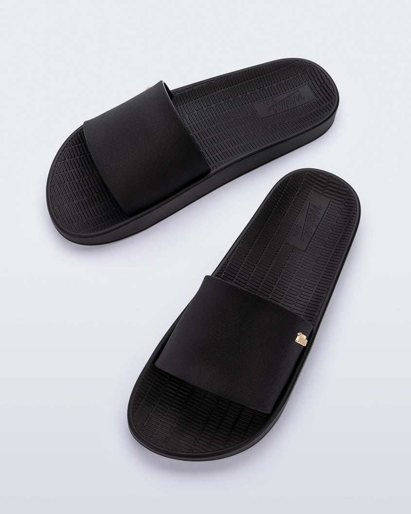 Top view of a pair of Melissa Sun Sunset slide sandals in black with gold Melissa logo on the top side corner of the strap. 