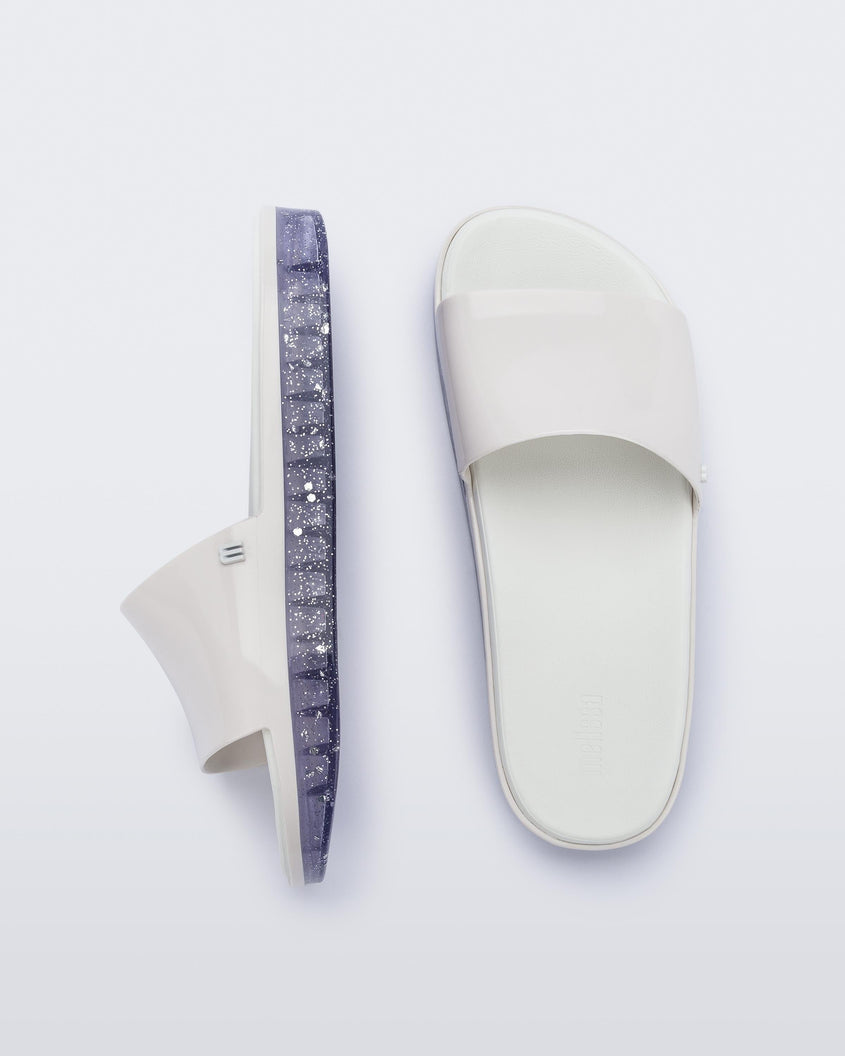 Top and side view of a pair of white Melissa Beach slides with clear/glitter soles. 