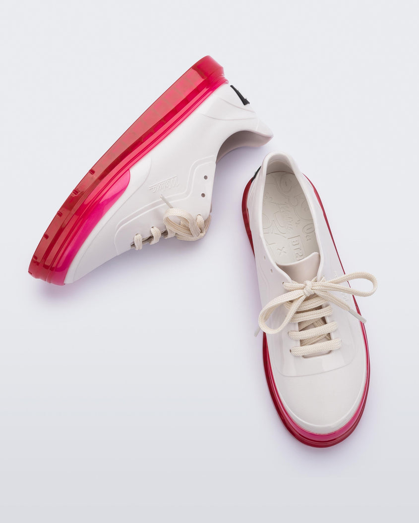 A top and side view of a pair of white Melissa Classic sneakers with a white base, laces, pink sole and a melissa logo on the side.