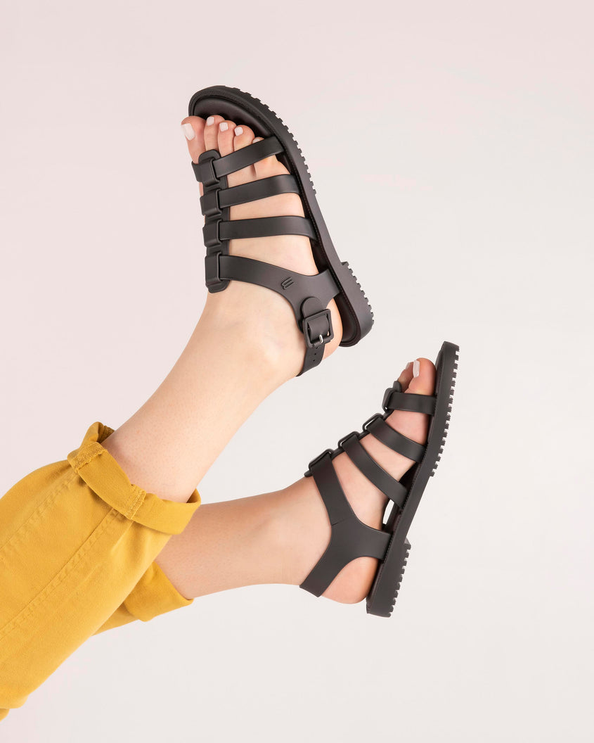 A model's legs wearing a pair of black Melissa Flox sandals with straps.