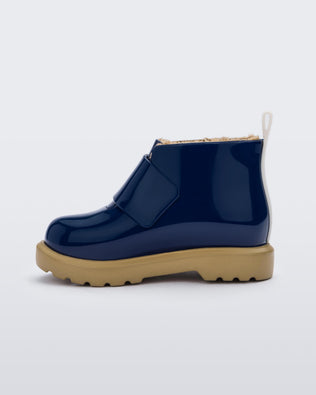 An inner side view of a blue/beige Mini Melissa Chelsea blue boots with a velcro strap, dark blue base, beige sole and beige fuzzy lining.