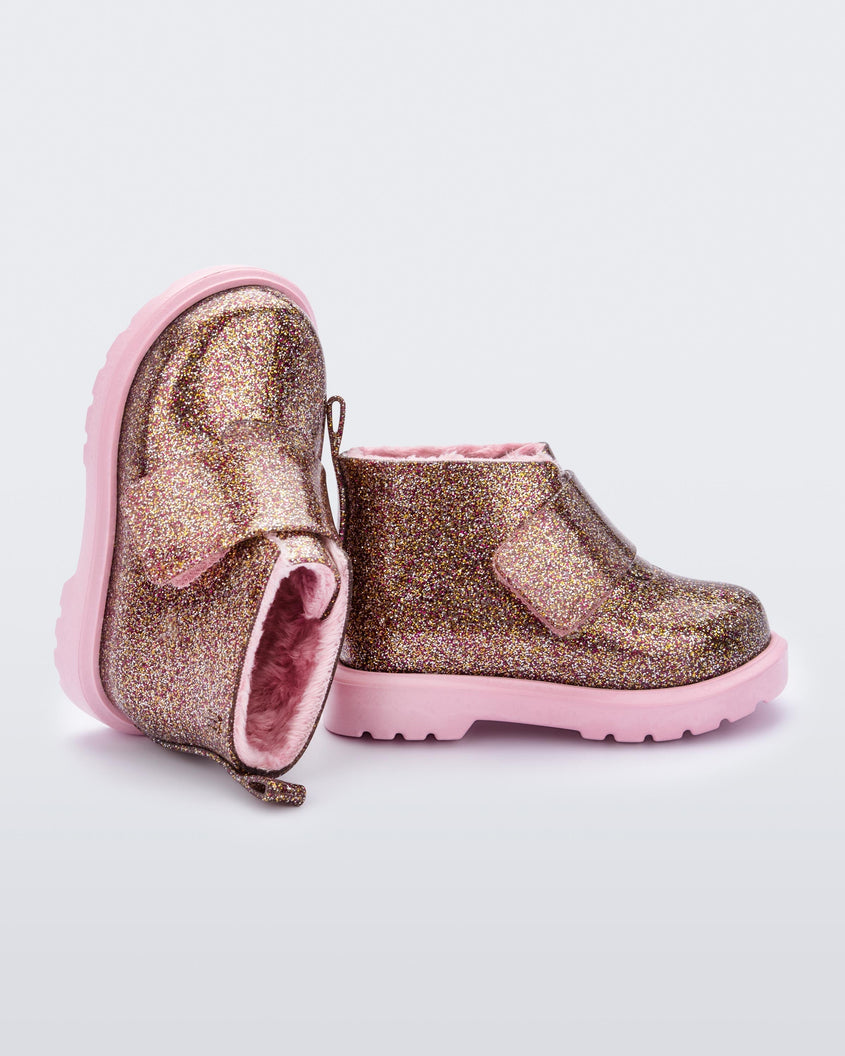 An angled top and side view of a pair of pink/glitter multicolor Mini Melissa Chelsea boots with a multicolor glitter base, velcro front strap and a pink sole.