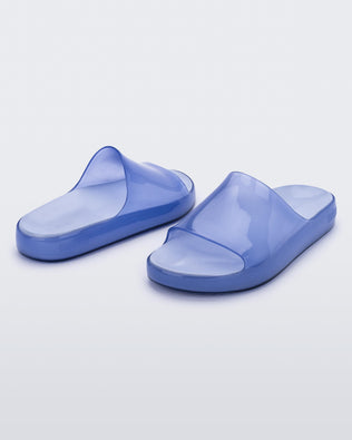 An angled front and back view of a pair of transparent blue Melissa Cloud slides.