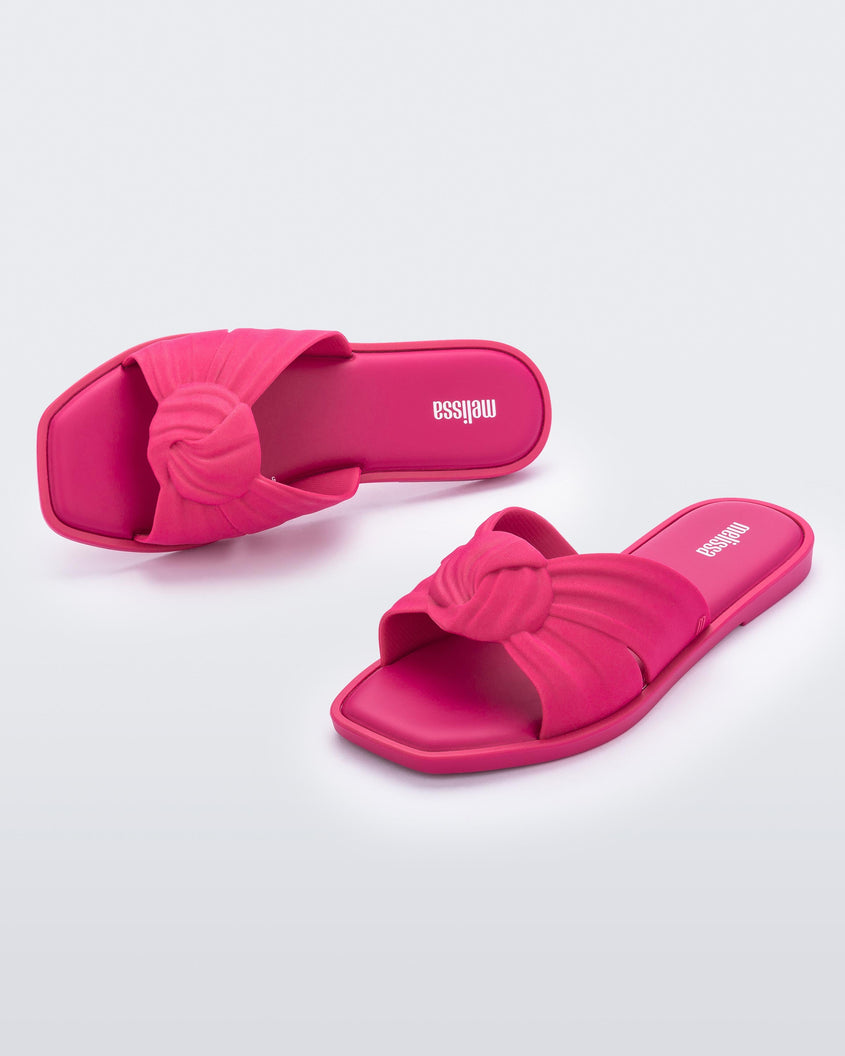 An angled front and top view of a pair of pink Melissa Plush slides with a twist front strap detail.