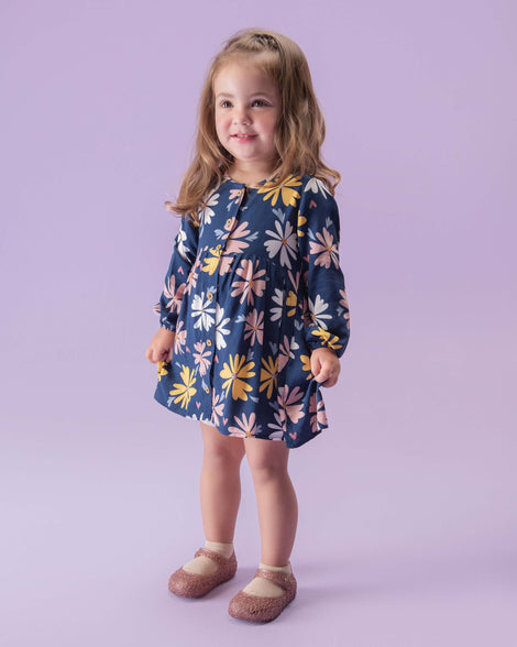 A child model wearing a floral printed dress with a pair of Mini Melissa Campana flats in rose glitter with an open woven texture.