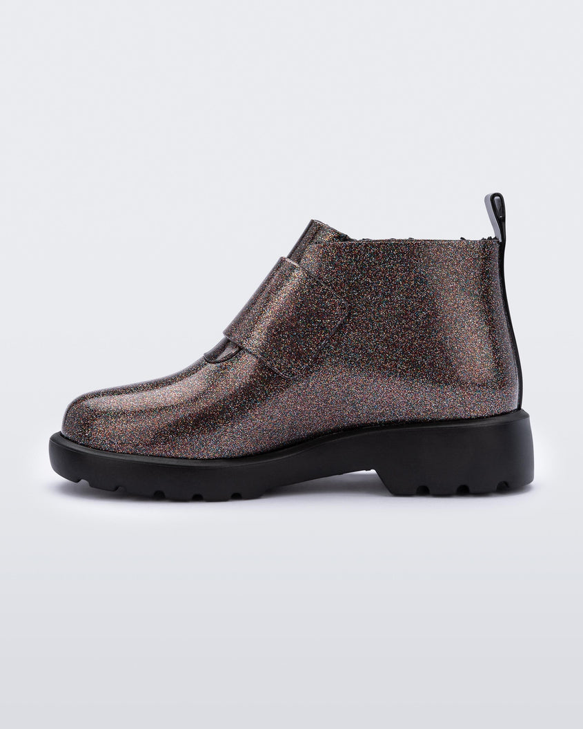 An inner side view of a black/glitter multicolor Mini Melissa Chelsea boot with a glitter multicolor base, velcro front strap and black sole.