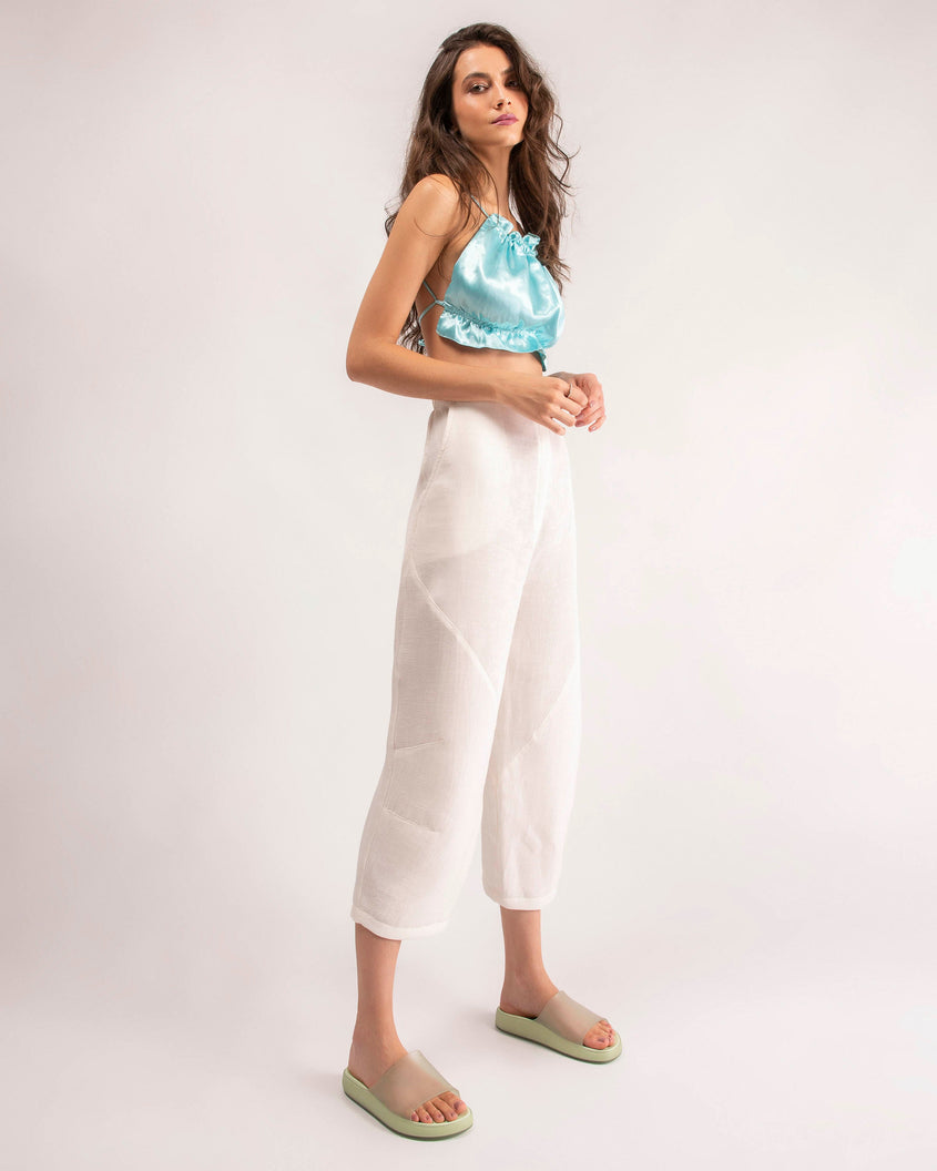 A model posing for a picture wearing a blue top, white pants and a pair of transparent green Melissa Cloud slides.