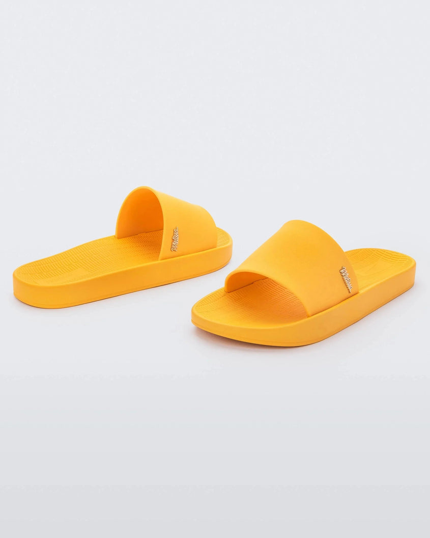 An angled front and back view of a pair of yellow Melissa Sun Sunset slides with a melissa logo on the side.