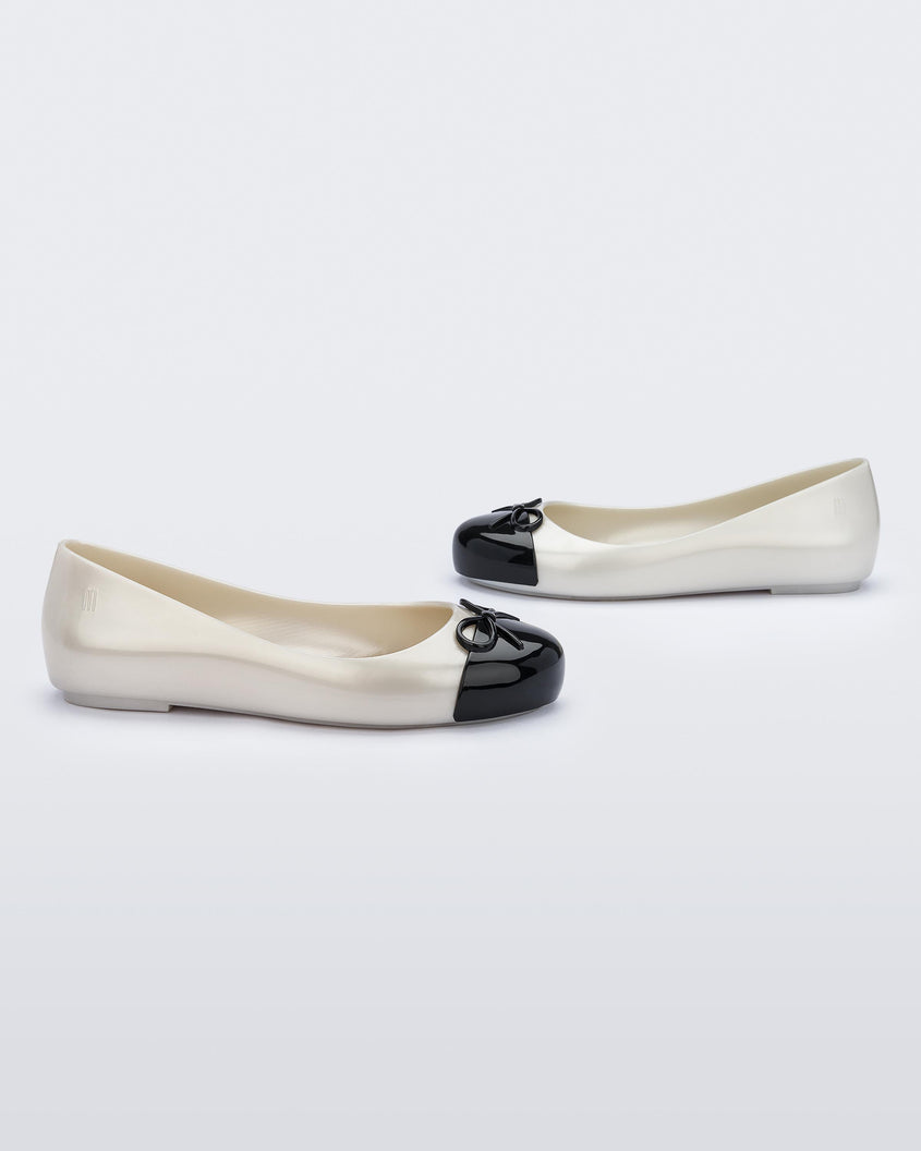 A side view of a pair of white Mini Melissa Sweet Love Cap Toe flats with a white base and a black toe cap with a bow on top.