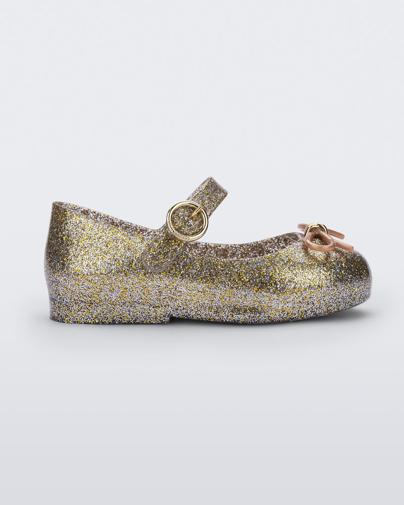 Side view of a Gold/Silver/Glitter Mini Melissa Sweet Love flat with a top strap and a bow detail on the toe.