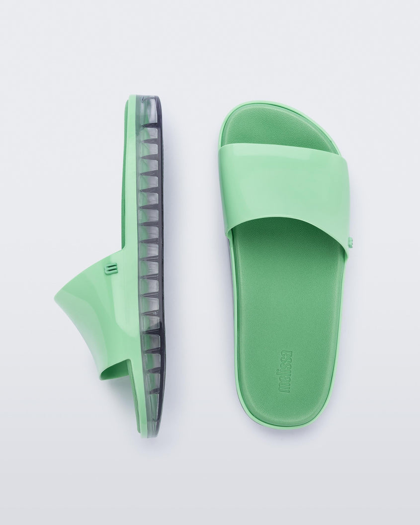 Top and side view of a pair of green Melissa Beach slides with clear soles. 