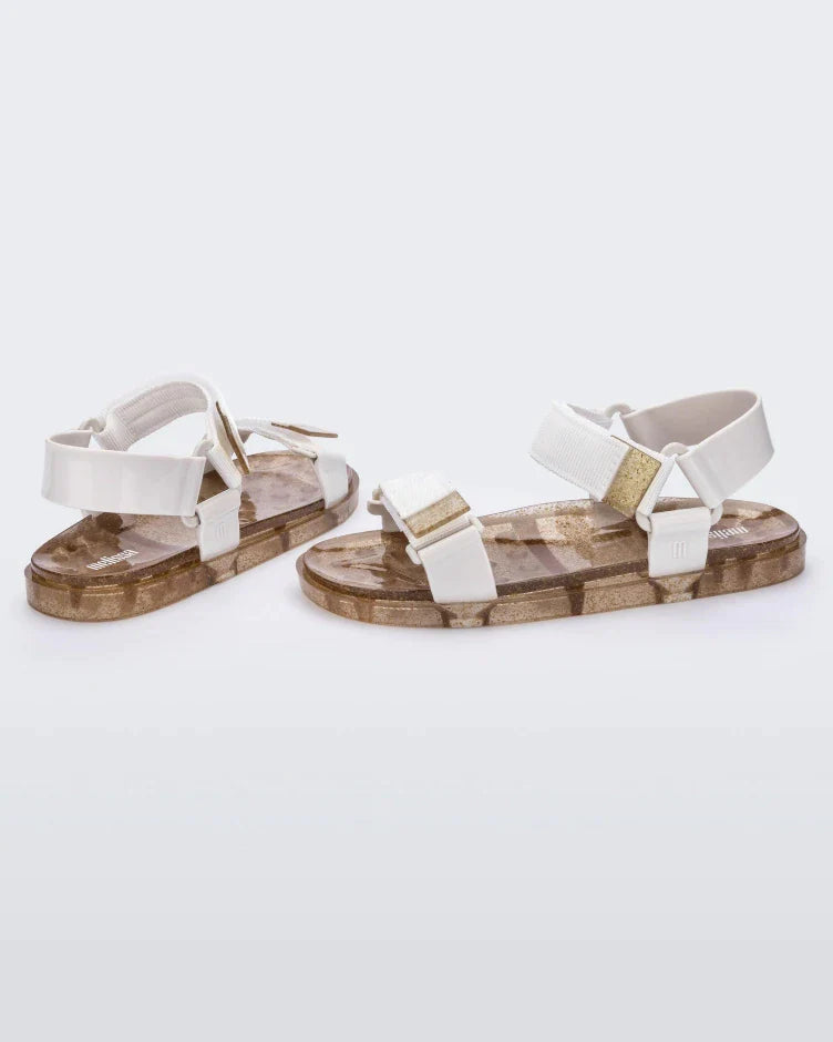 Angled view of a pair of Melissa Wide Papete sandals with gold glitter sole and white velcro straps