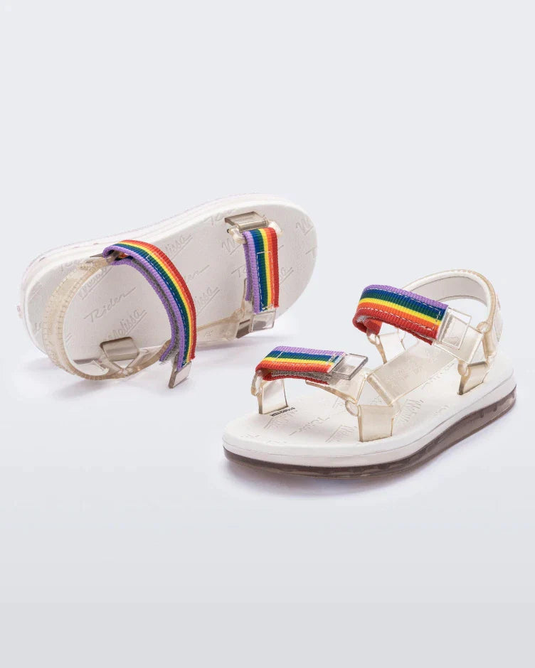Angled view of a pair of white Mini Melissa Papete sandals with rainbow straps.
